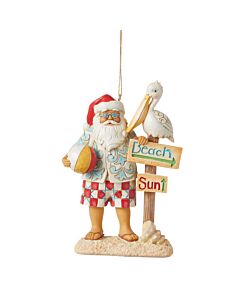 The Santa with Signs and Pelican Ornament depicts a festive beach-ready Santa in patchwork swim trunks and a Hawaiian shirt, accompanied by a guiding pelican. This Jim Shore collectible adds playful coastal charm and holiday cheer to any tree.