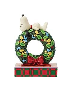 Jim Shore’s Lighted Happy Holiday Dreams figurine featuring Snoopy napping atop a festive holiday wreath, while a group of cheerful Woodstocks decorates with playful charm and seasonal cheer.