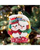 Christopher Radko 'A Picture Perfect Pair' ornament features two cheerful snowmen smiling for the camera, framed in gold and tied with a festive bow. This glass ornament adds a charming and whimsical touch to your holiday decorations.