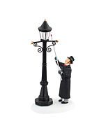 A lamplighter reaches up to ignite a gas streetlamp, bringing warm light to a wintry village lane.