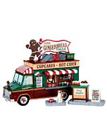 Charming holiday scene featuring a festive food truck crammed with cupcakes, cider, and gingerbread treats, accompanied by a playful dog with a bowl and a delightful free samples display.